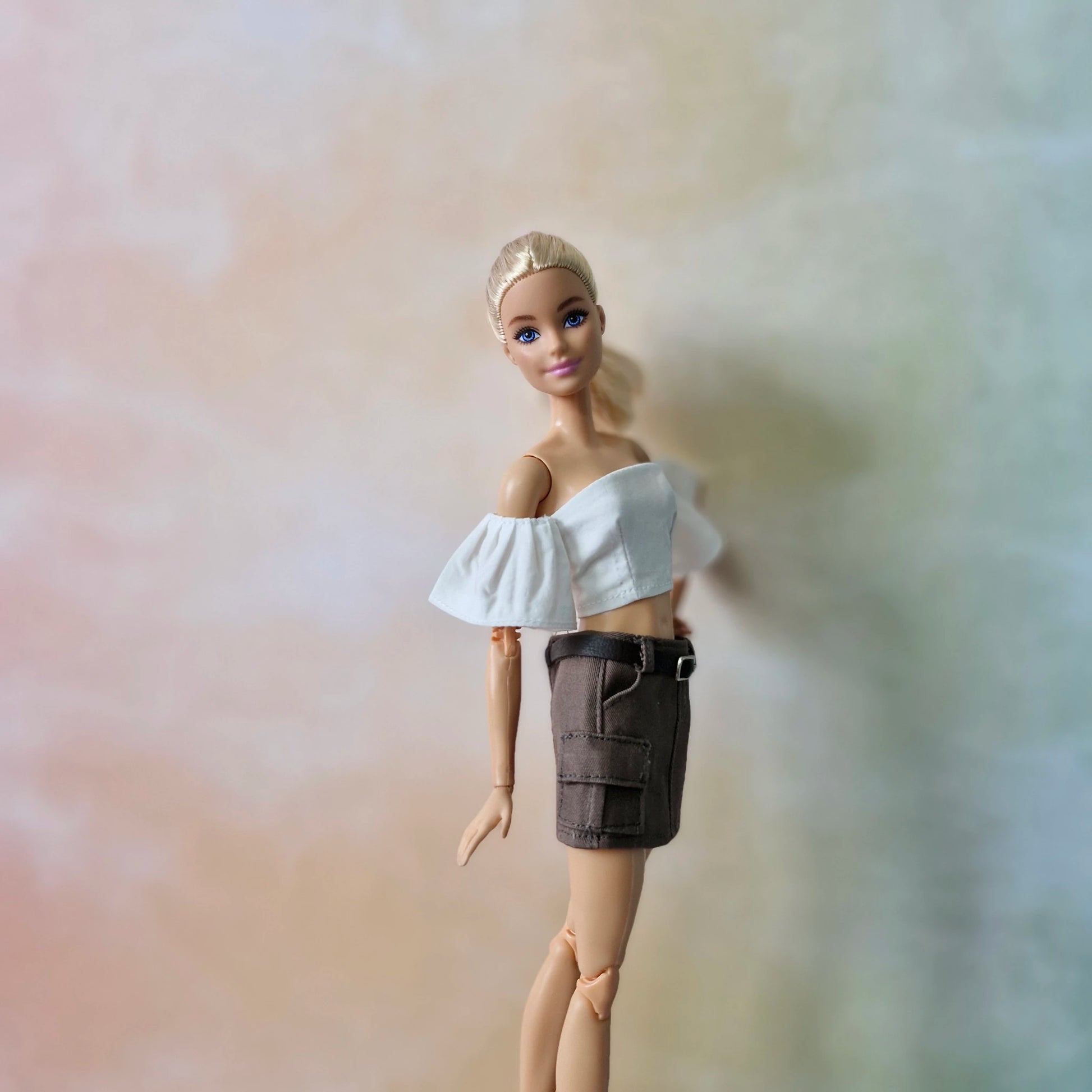 Close-up of blonde Barbie wearing white off-shoulder top and brown utility mini skirt.