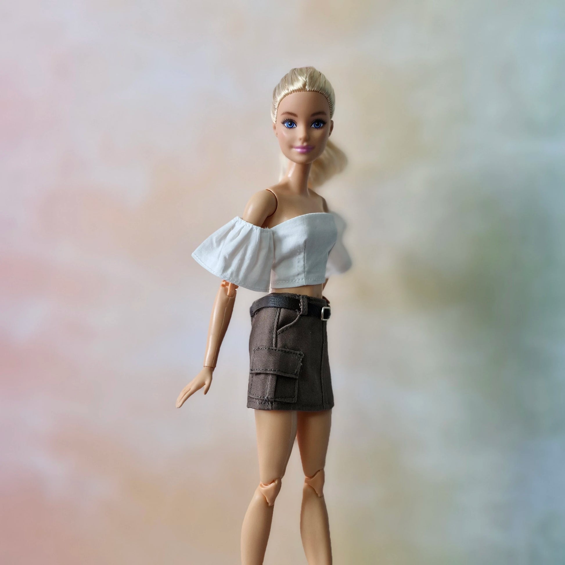 Side view of Barbie doll in white ruffled sleeve crop top and brown cargo mini skirt.
