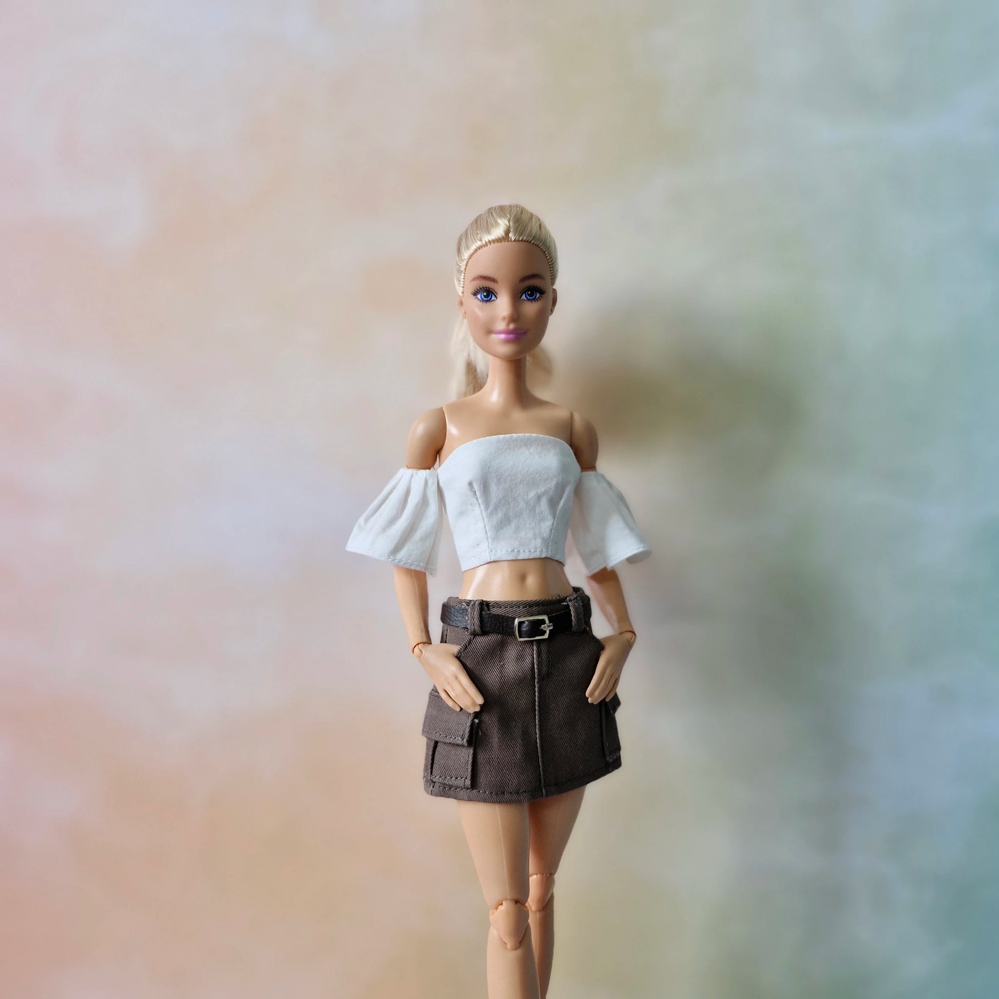 Blonde Barbie doll models white off-shoulder crop top and brown cargo mini skirt.