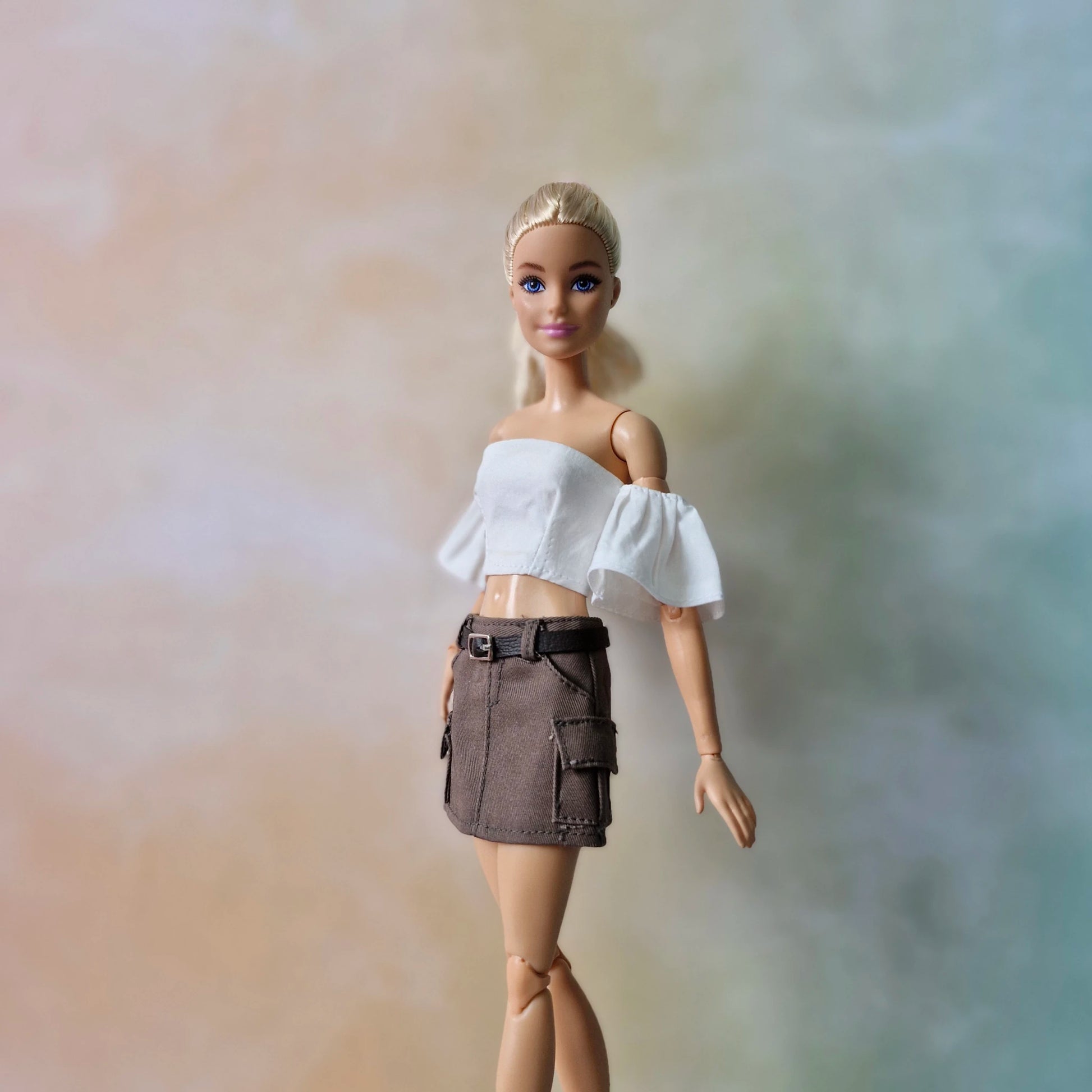Blonde Barbie doll posing in white off-shoulder top and brown belted cargo skirt.