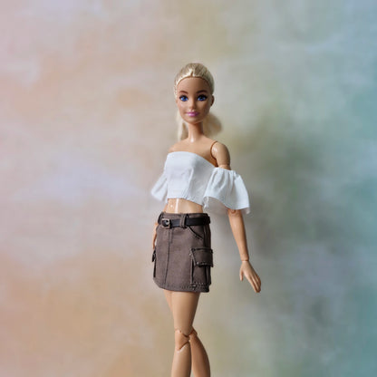 Blonde Barbie doll posing in white off-shoulder top and brown belted cargo skirt.