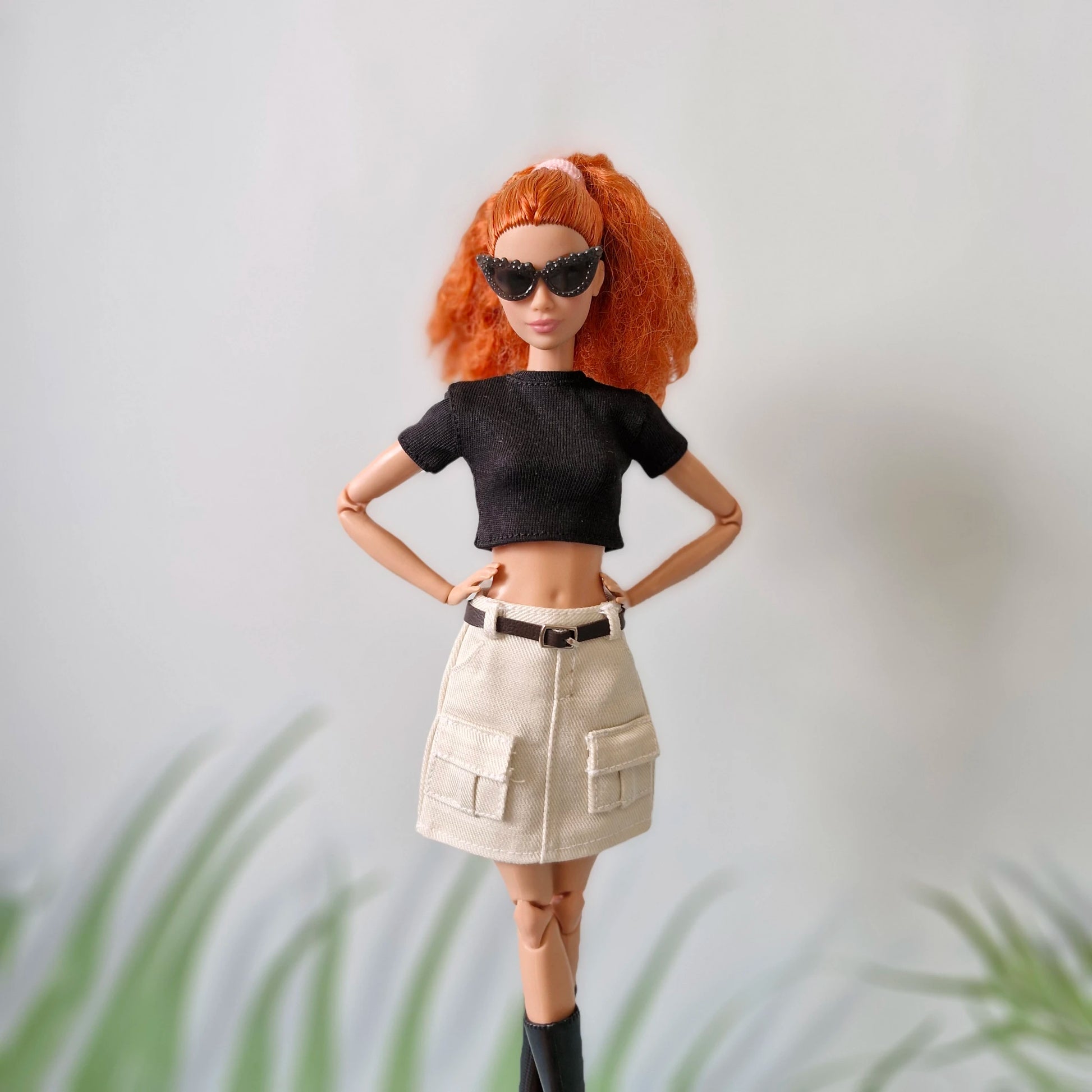 Fashion Barbie doll with red hair wearing a black top, white belted cargo skirt, and sunglasses, showing off her modern style.
