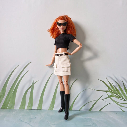 Red-haired Barbie doll wearing a black crop top, white cargo mini skirt, black boots, and sunglasses, posing with hands on hips