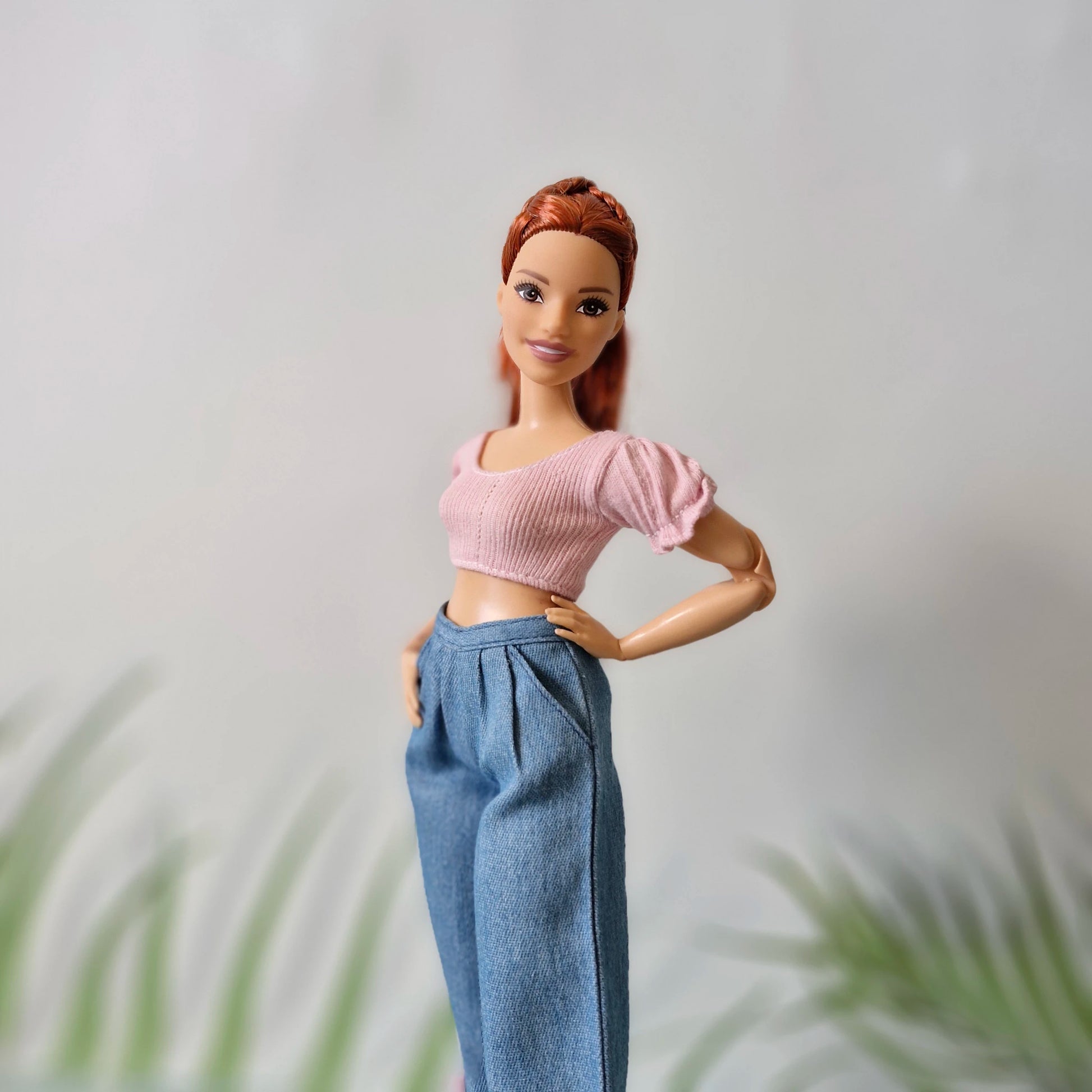 Red-haired Barbie doll smiling in a pink puff-sleeve crop top and high-waisted wide-leg blue jeans.