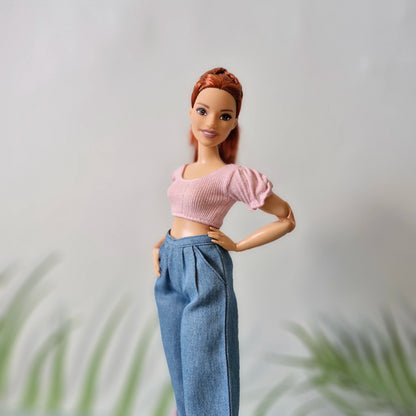 Red-haired Barbie doll smiling in a pink puff-sleeve crop top and high-waisted wide-leg blue jeans.