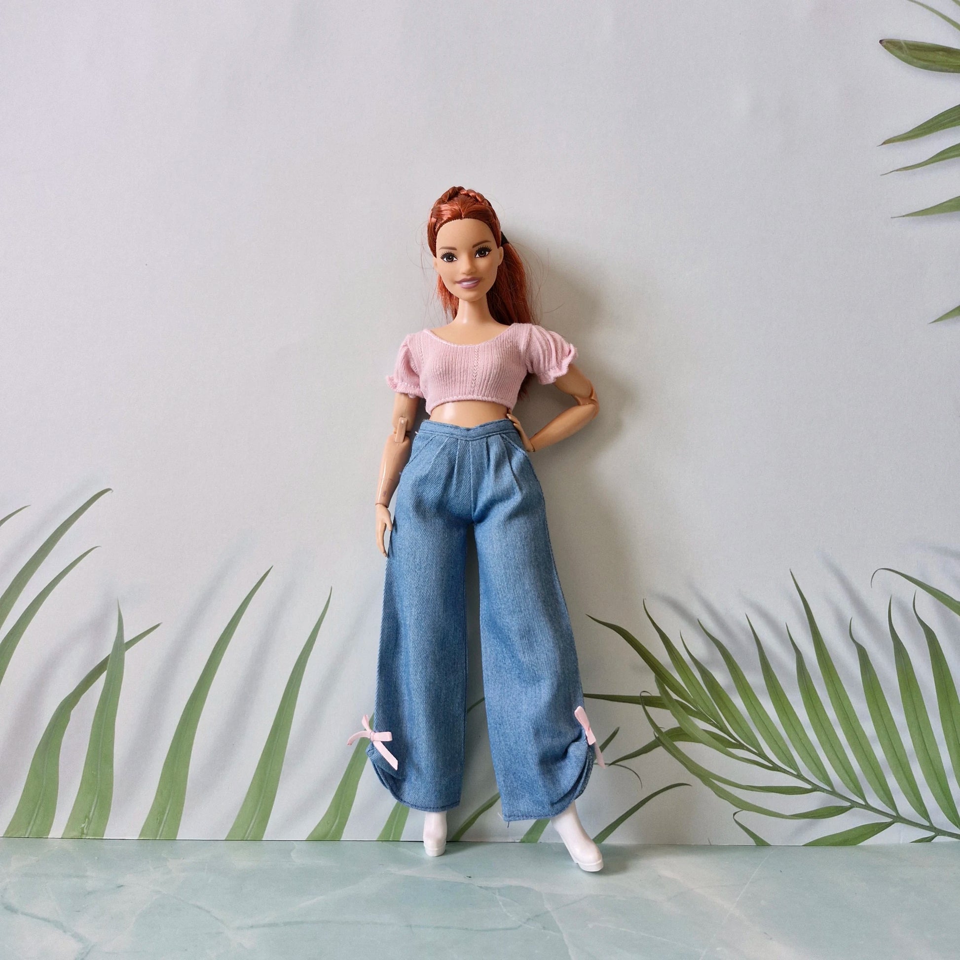 Full view of a red-haired Barbie doll wearing a pink crop top and wide-leg blue jeans with pink bows at the ankles.