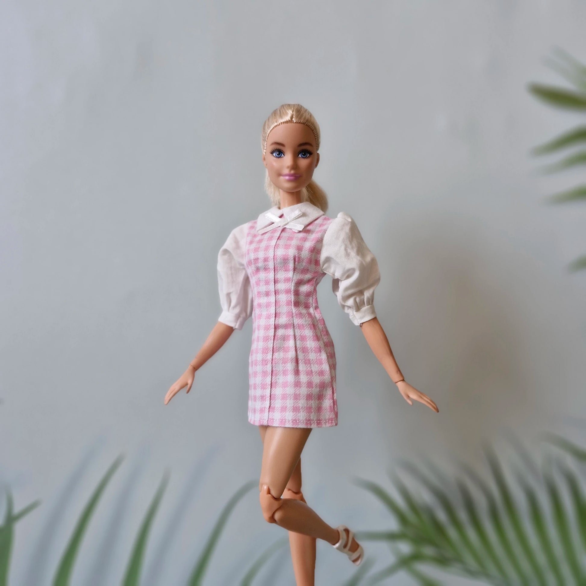 Blonde Barbie doll posing in a pink gingham dress and white heeled sandals, showing the full handmade outfit