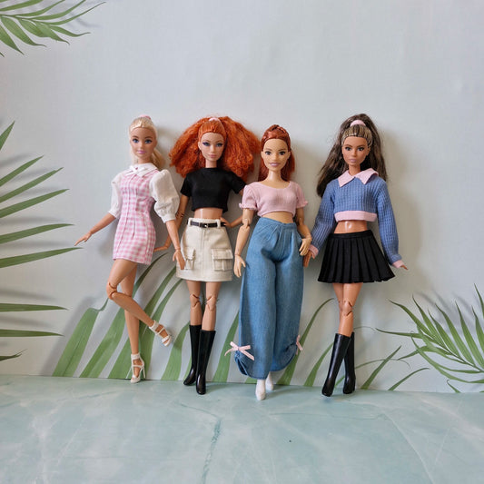 Four Barbie dolls standing together showcasing a collection of trendy handmade outfits including a dress, skirts, and jeans.