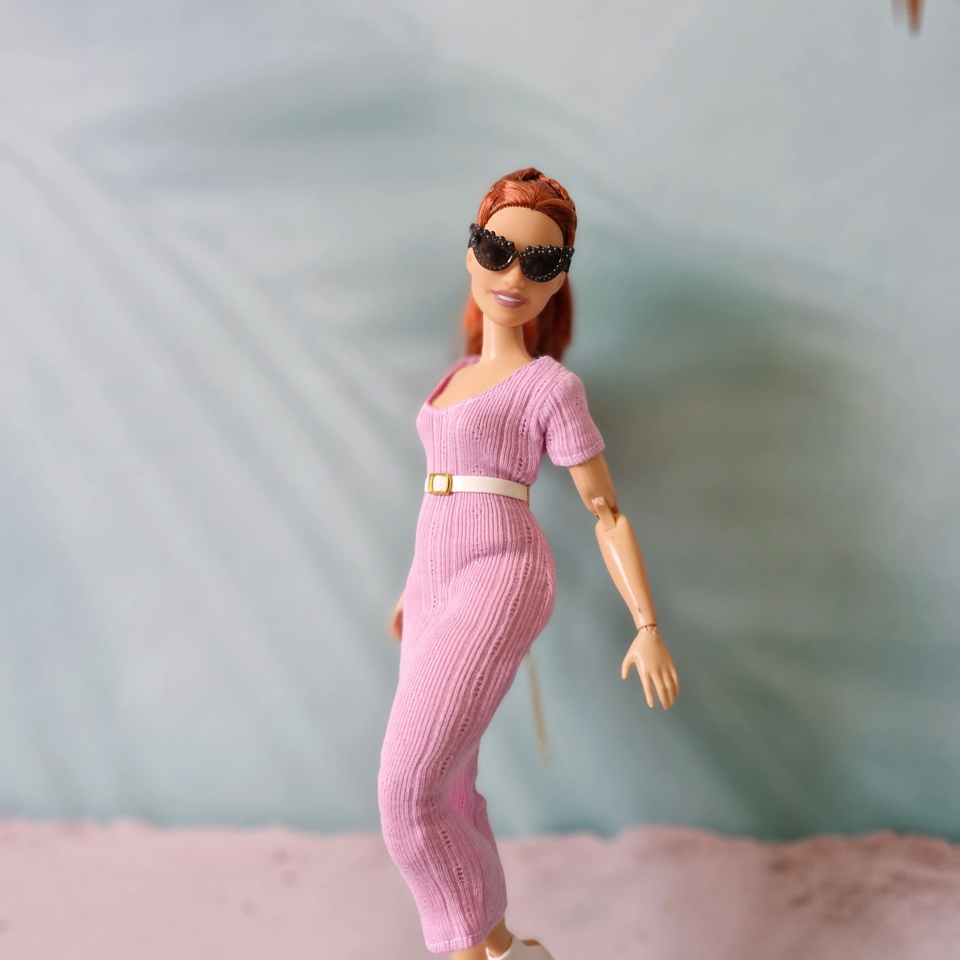 Side view of Barbie doll in pink ribbed midi dress and white belt, wearing white boots and sunglasses.