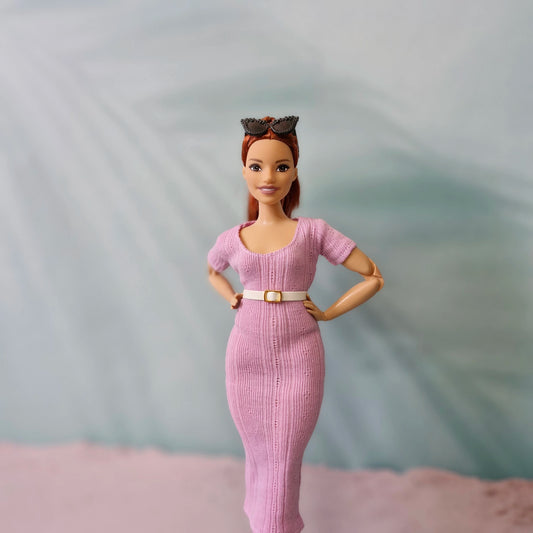 Red-haired Barbie doll in pink ribbed midi dress with a white belt, sunglasses on her head.