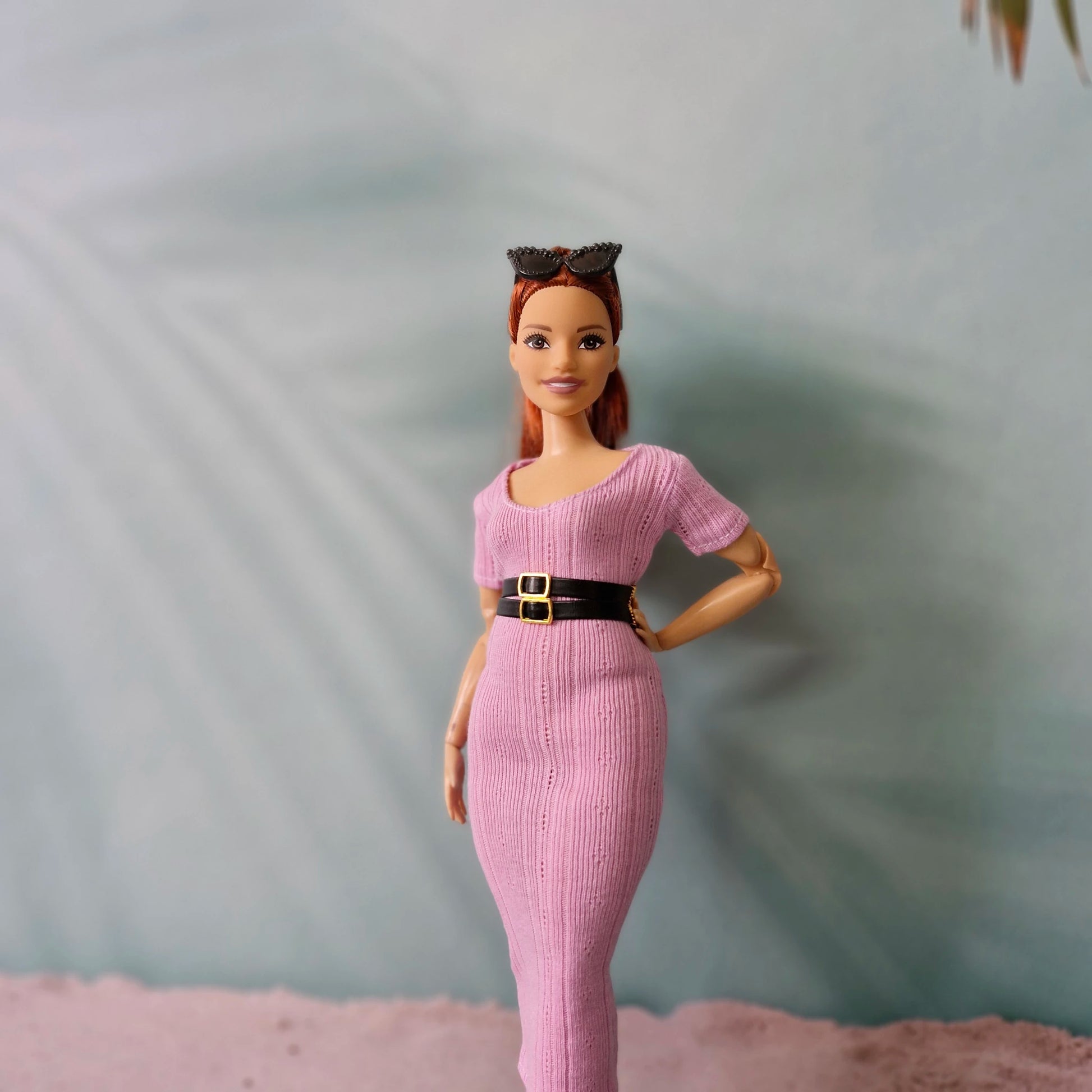 Barbie doll models pink ribbed midi dress accessorized with a wide black belt and sunglasses on head.