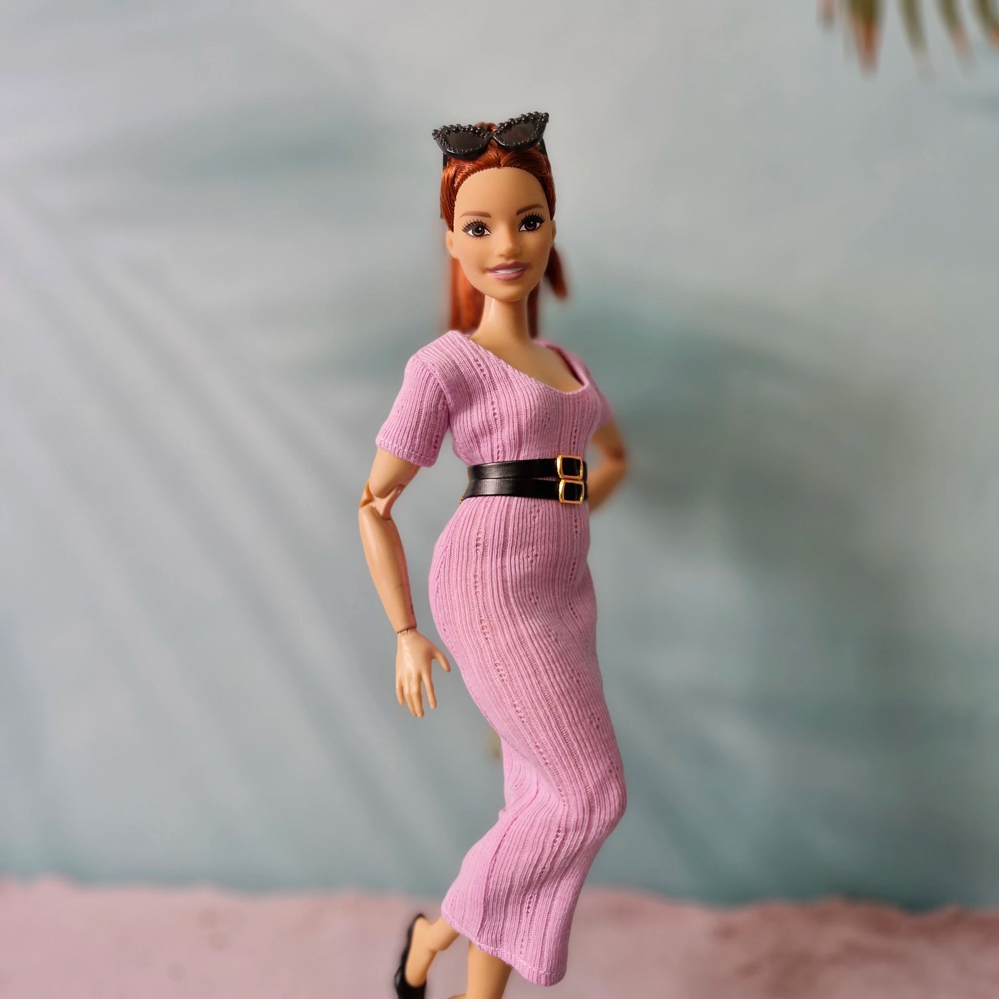 Barbie doll posing in pink ribbed dress with black belt and black shoes, side view.