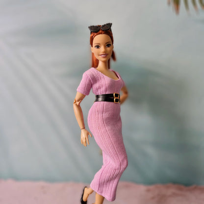 Barbie doll posing in pink ribbed dress with black belt and black shoes, side view.