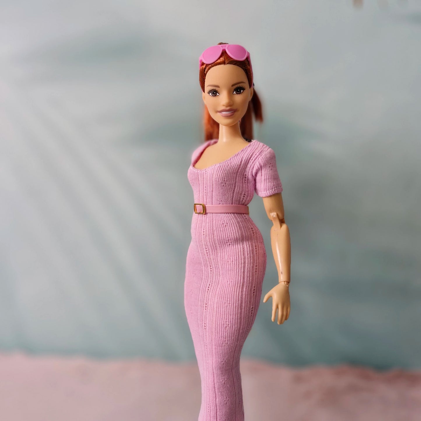 Close-up of Barbie doll in pink ribbed dress and matching thin pink belt, sunglasses on head.