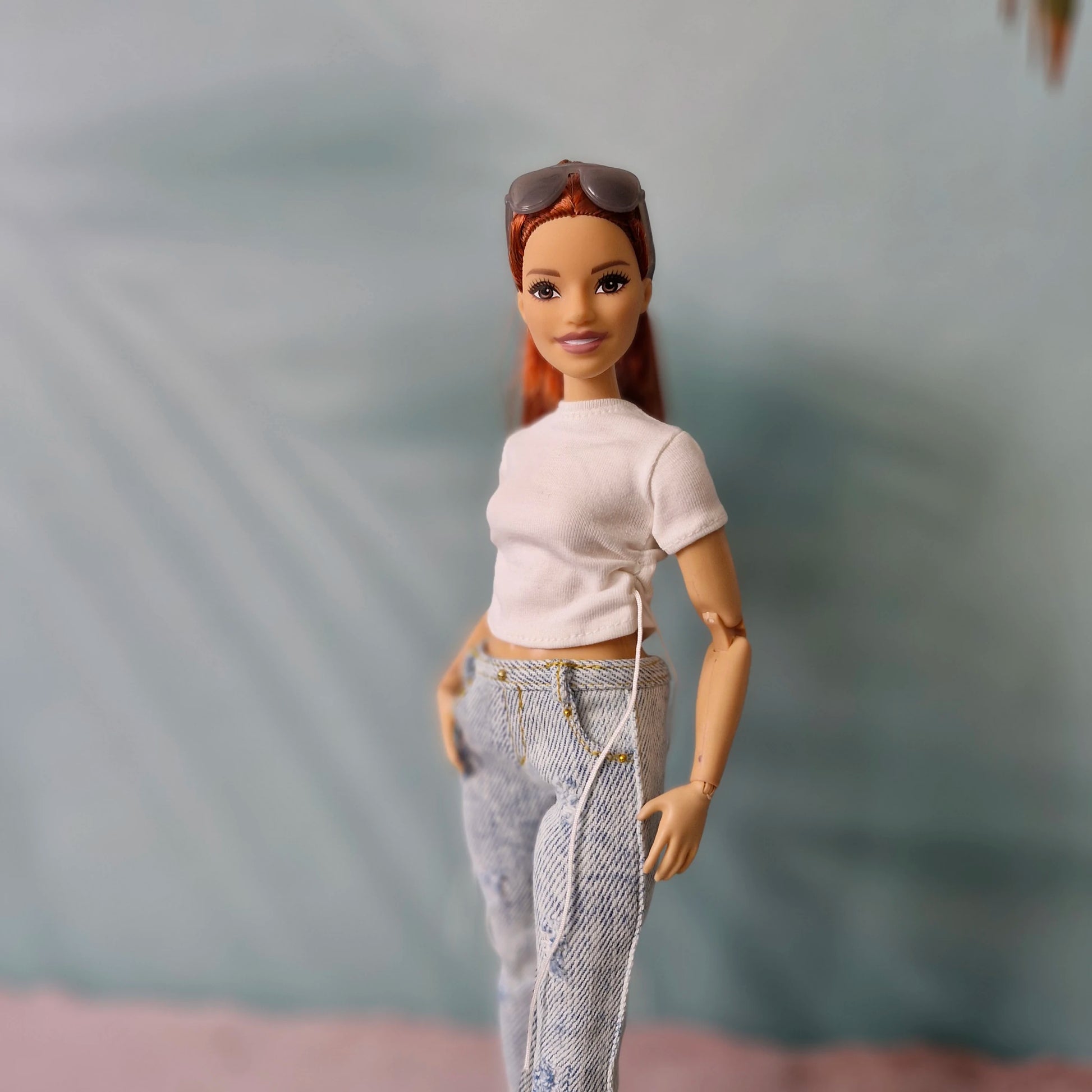 Portrait of a smiling curvy redhead Barbie doll with sunglasses on her head, modeling a white t-shirt and light-wash jeans.