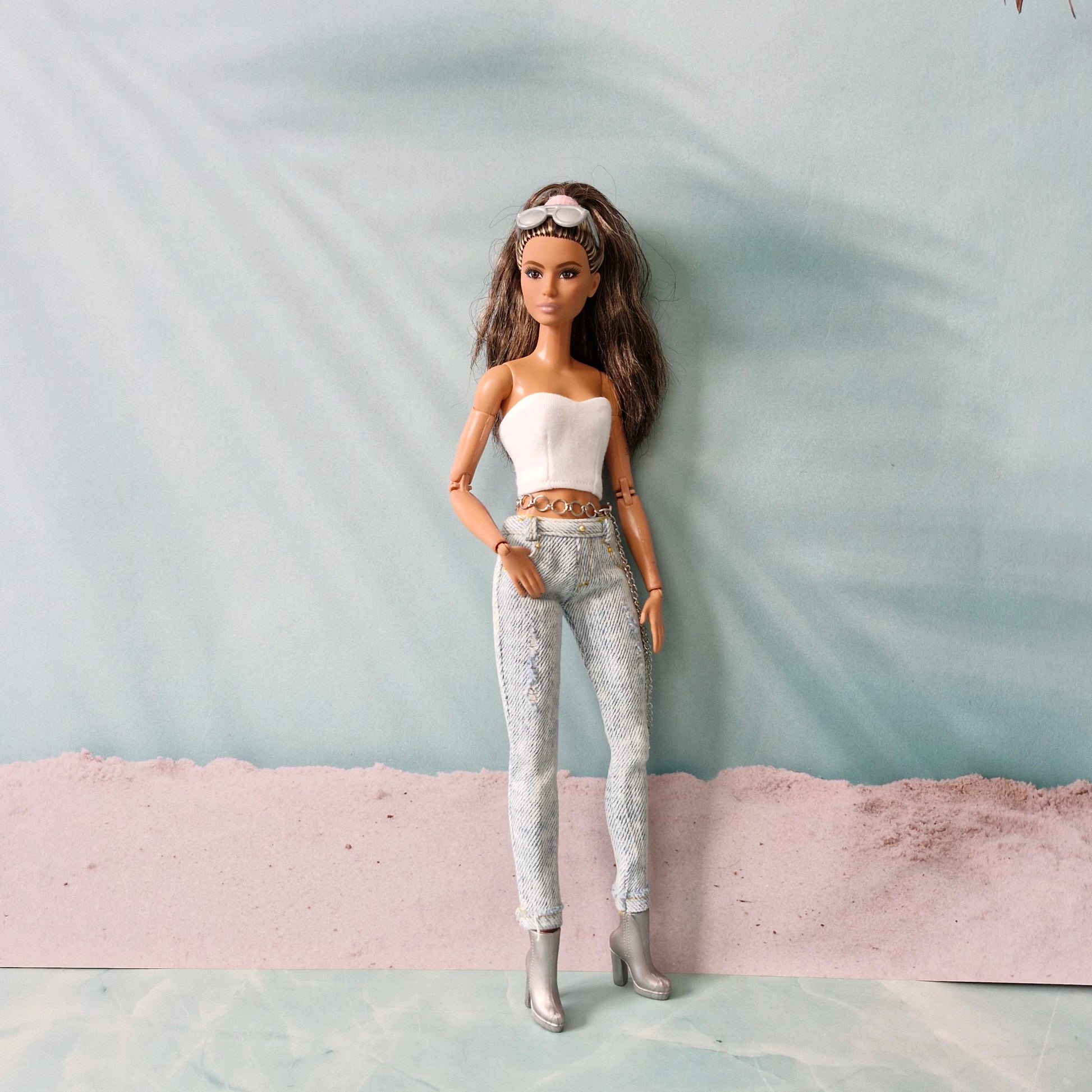 Full-length view of a brunette Barbie doll in a white tube top, distressed jeans, and silver boots, standing confidently.