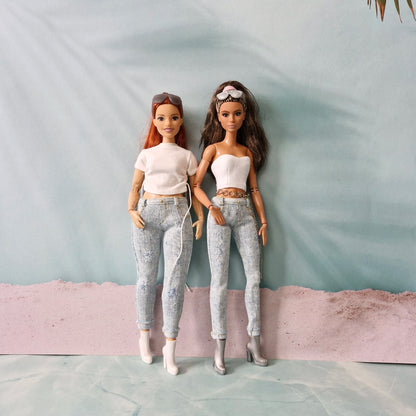 Two Barbie dolls, a curvy redhead and a brunette, side-by-side wearing matching light-wash distressed jeans and white tops.