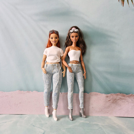 Two Barbie dolls, a curvy redhead and a brunette, side-by-side wearing matching light-wash distressed jeans and white tops.