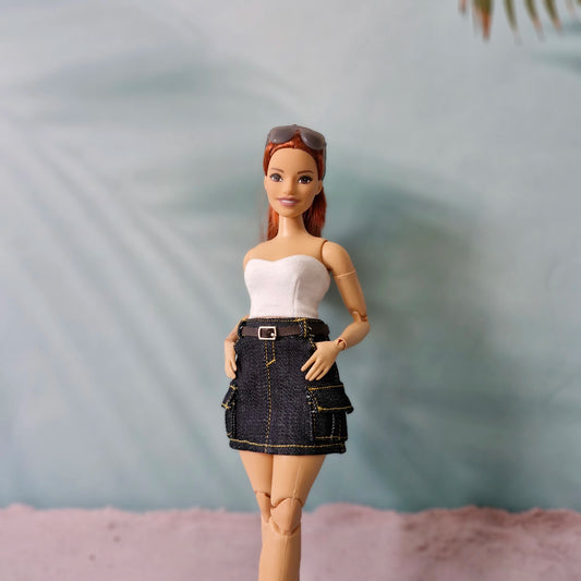 Barbie doll wearing a white top and denim skirt with sunglasses on head against a blurred background