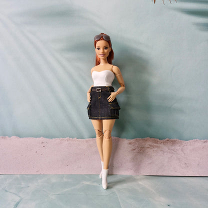 Barbie doll wearing a white top and denim skirt with a gray background