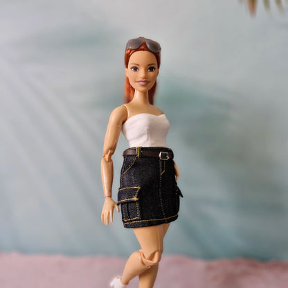Barbie doll wearing a white top and black denim skirt with sunglasses on head against a blurred background