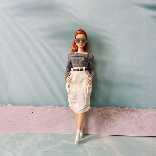 Barbie doll wearing a gray off-shoulder top and beige skirt against a plain background