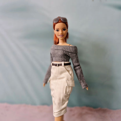 Barbie doll wearing a gray off-shoulder top and beige pants against a plain background