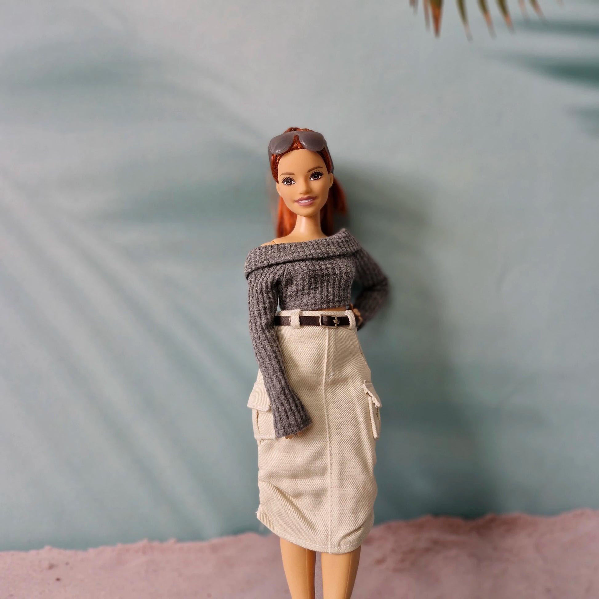 Barbie doll wearing a gray sweater and beige skirt against a neutral background
