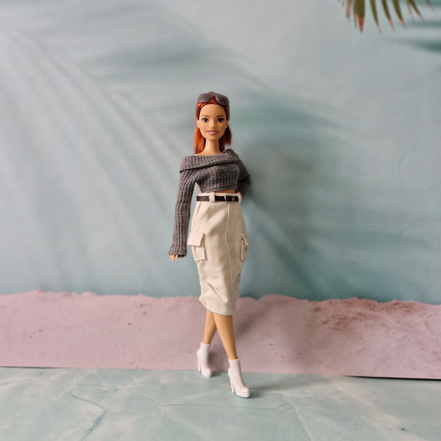 Barbie doll wearing a gray sweater and beige skirt on a light blue surface