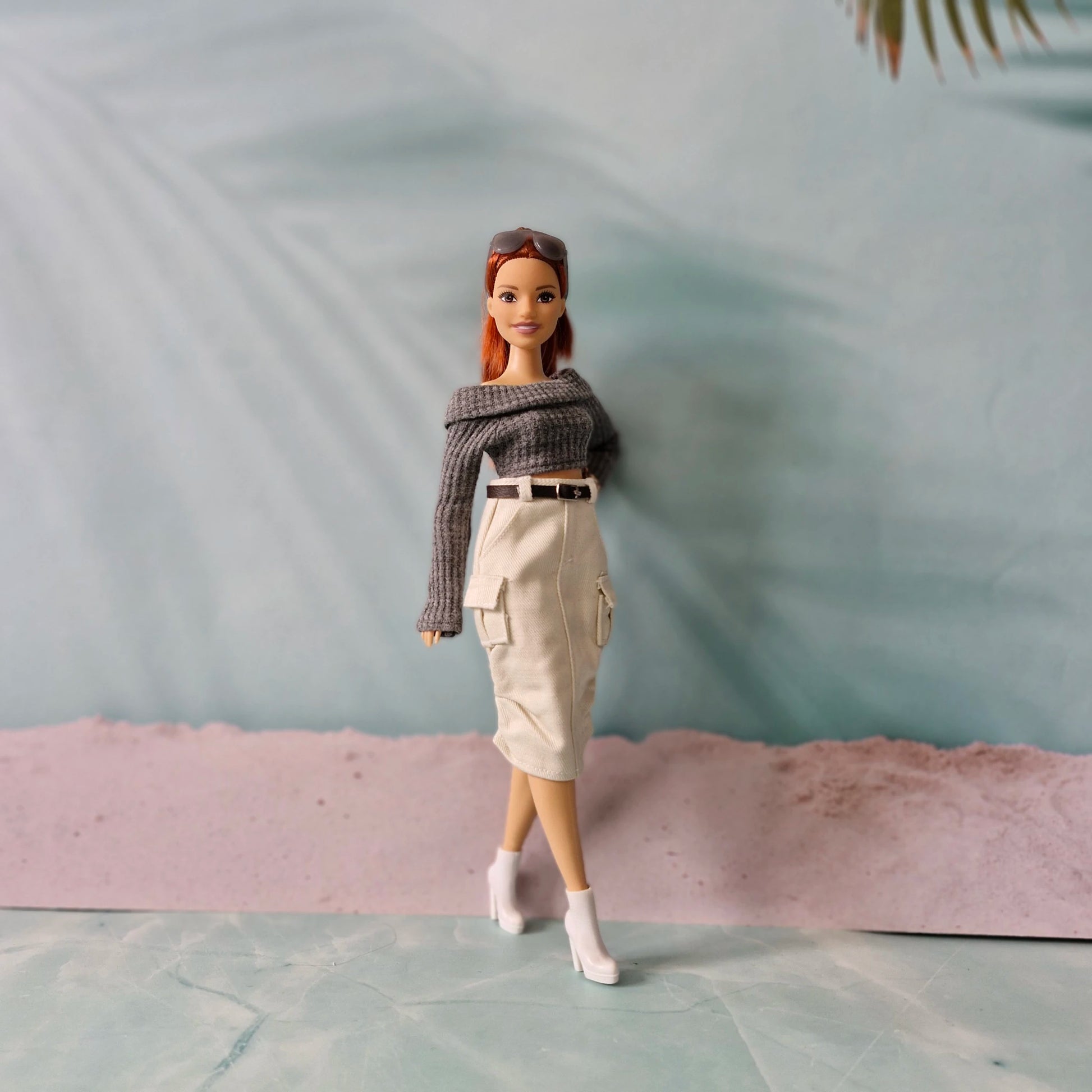 Barbie doll wearing a gray sweater and beige skirt on a light blue surface