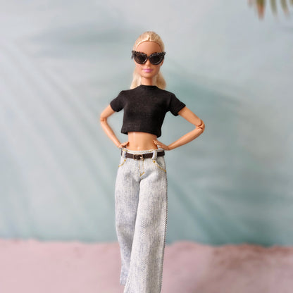Barbie doll wearing a black crop top and light-colored pants with sunglasses against a neutral background