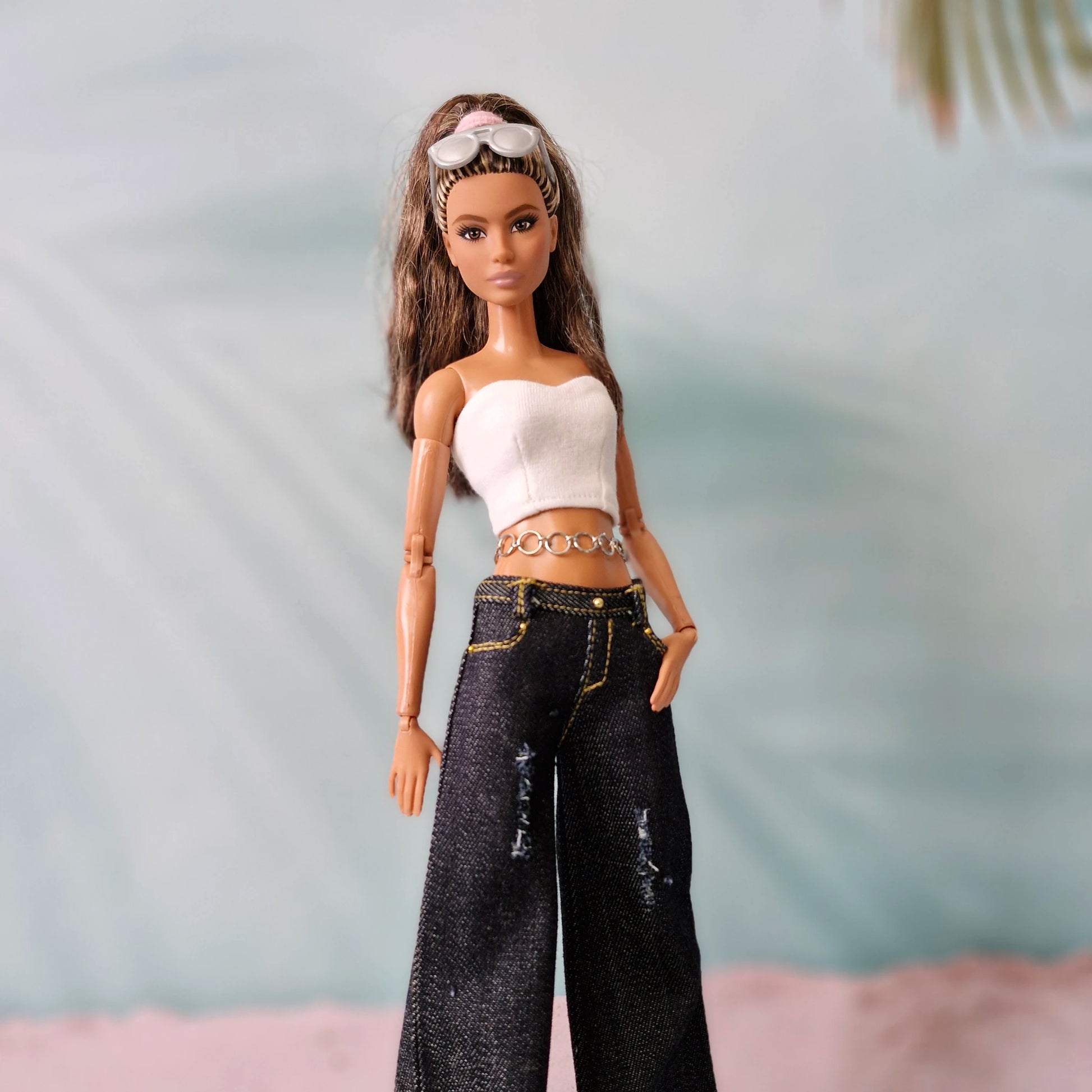 Close-up of Barbie doll in Y2K fashion: dark denim wide-leg jeans and a white bandeau top.