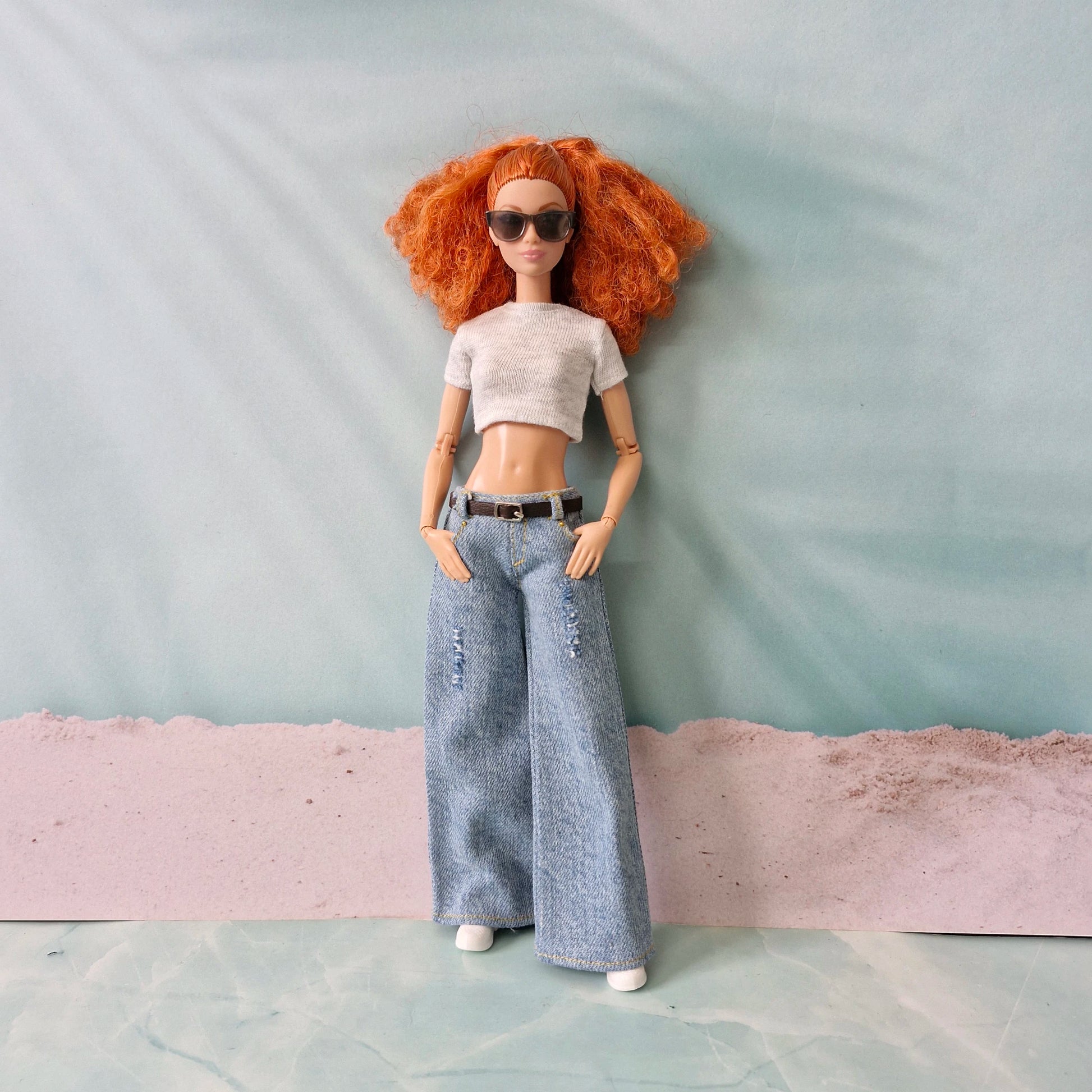 Red-haired Barbie doll wearing light blue wide-leg jeans, a white crop top, and sunglasses.