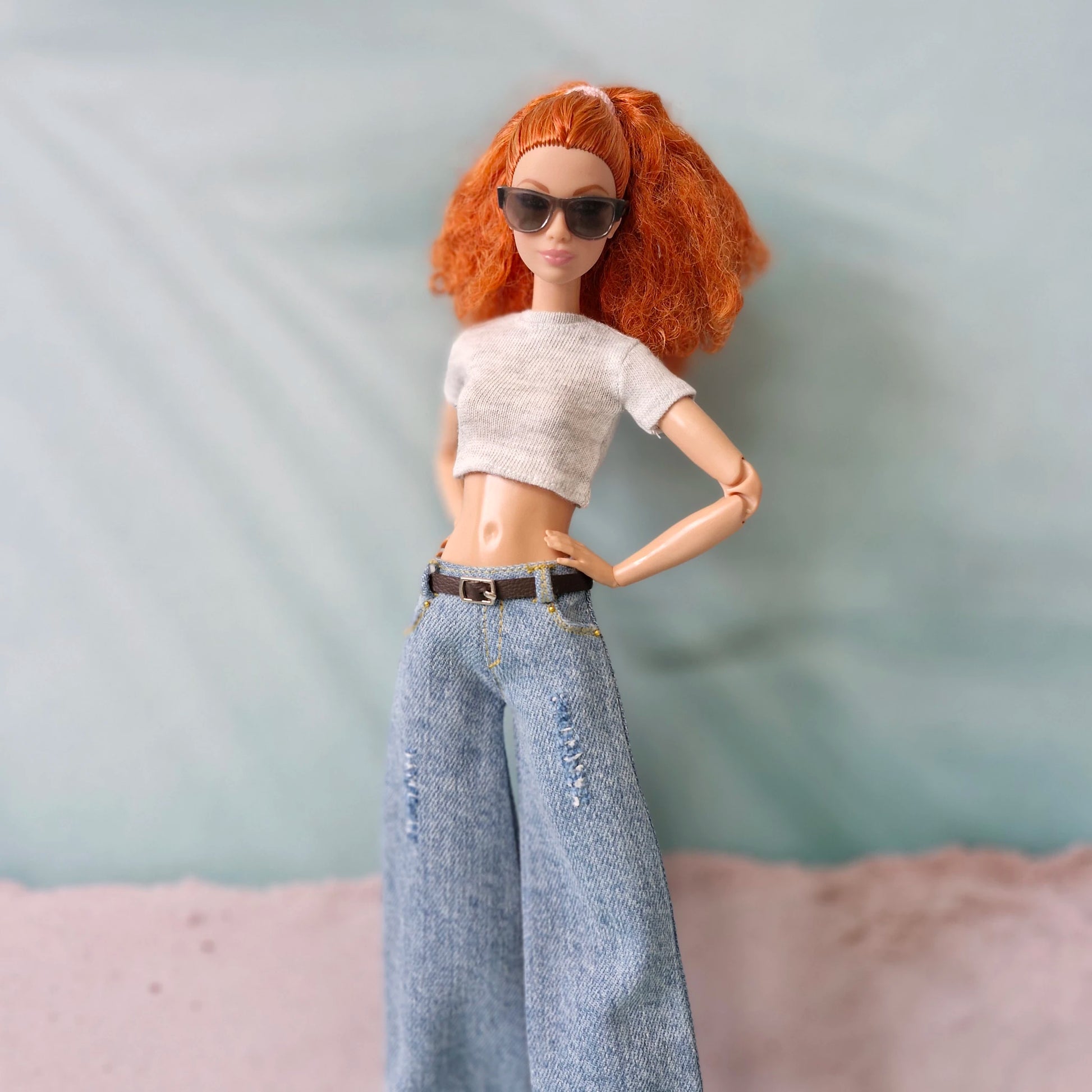 Close-up of red-haired Barbie doll in trendy wide-leg jeans and white crop top, posing with hand on hip.
