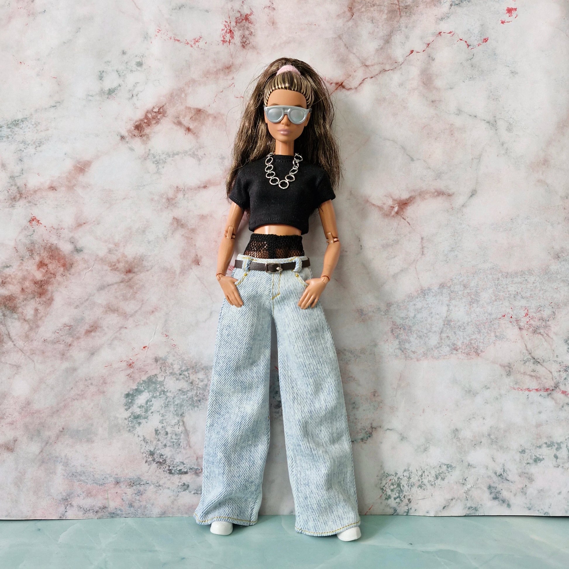 Barbie doll wearing sunglasses, a layered black crop top, and wide-leg jeans, with hands in pockets.
