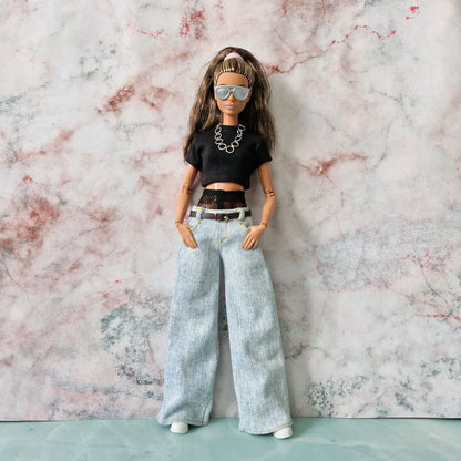 Barbie doll wearing sunglasses, a layered black crop top, and wide-leg jeans, with hands in pockets.