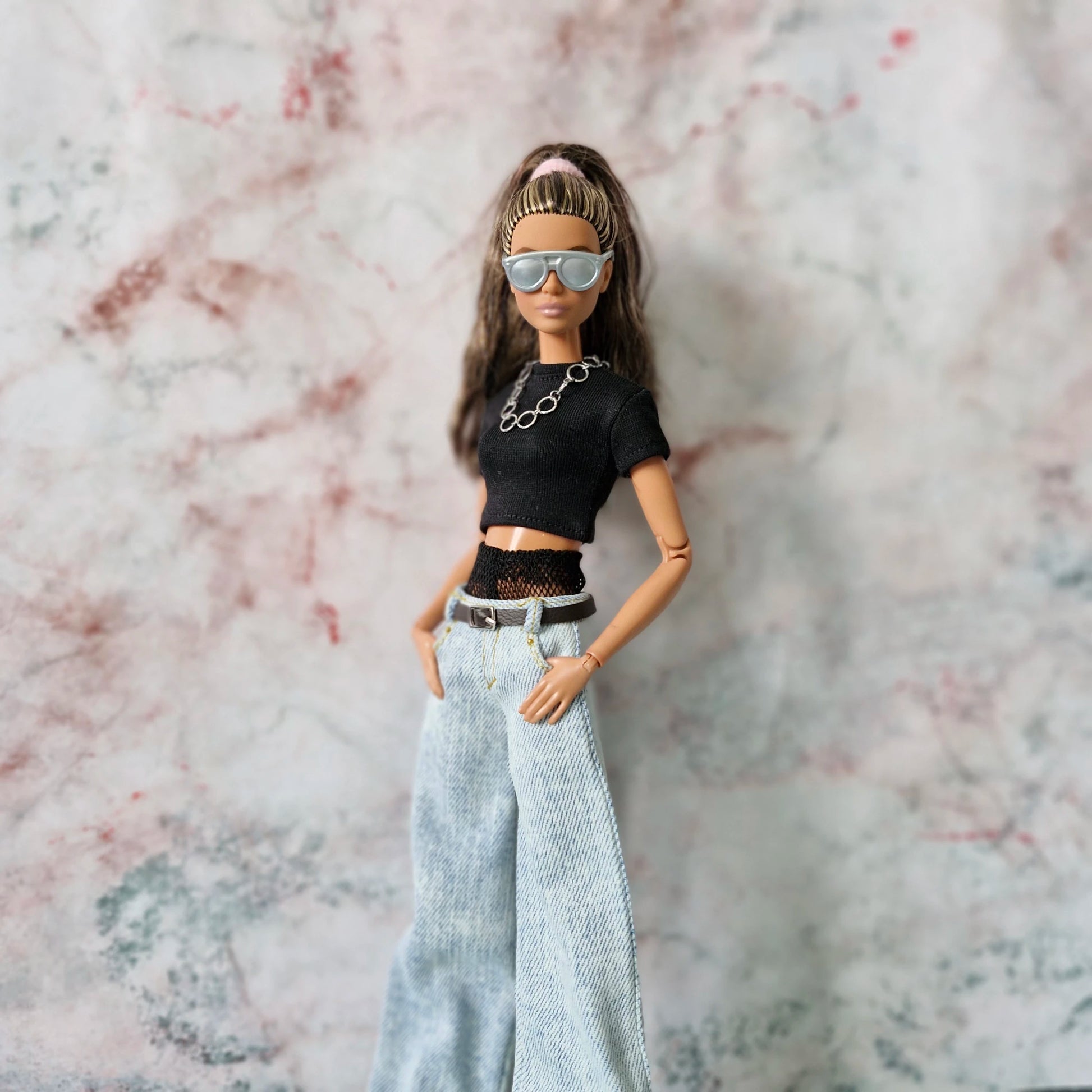 Close-up of Barbie doll in sunglasses and chain necklace, wearing a Y2K layered top and wide-leg jeans.