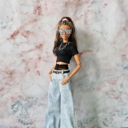 Close-up of Barbie doll in sunglasses and chain necklace, wearing a Y2K layered top and wide-leg jeans.