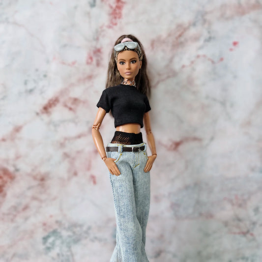 Barbie doll with hands in pockets, modeling Y2K outfit with layered crop top and light-wash wide-leg jeans.