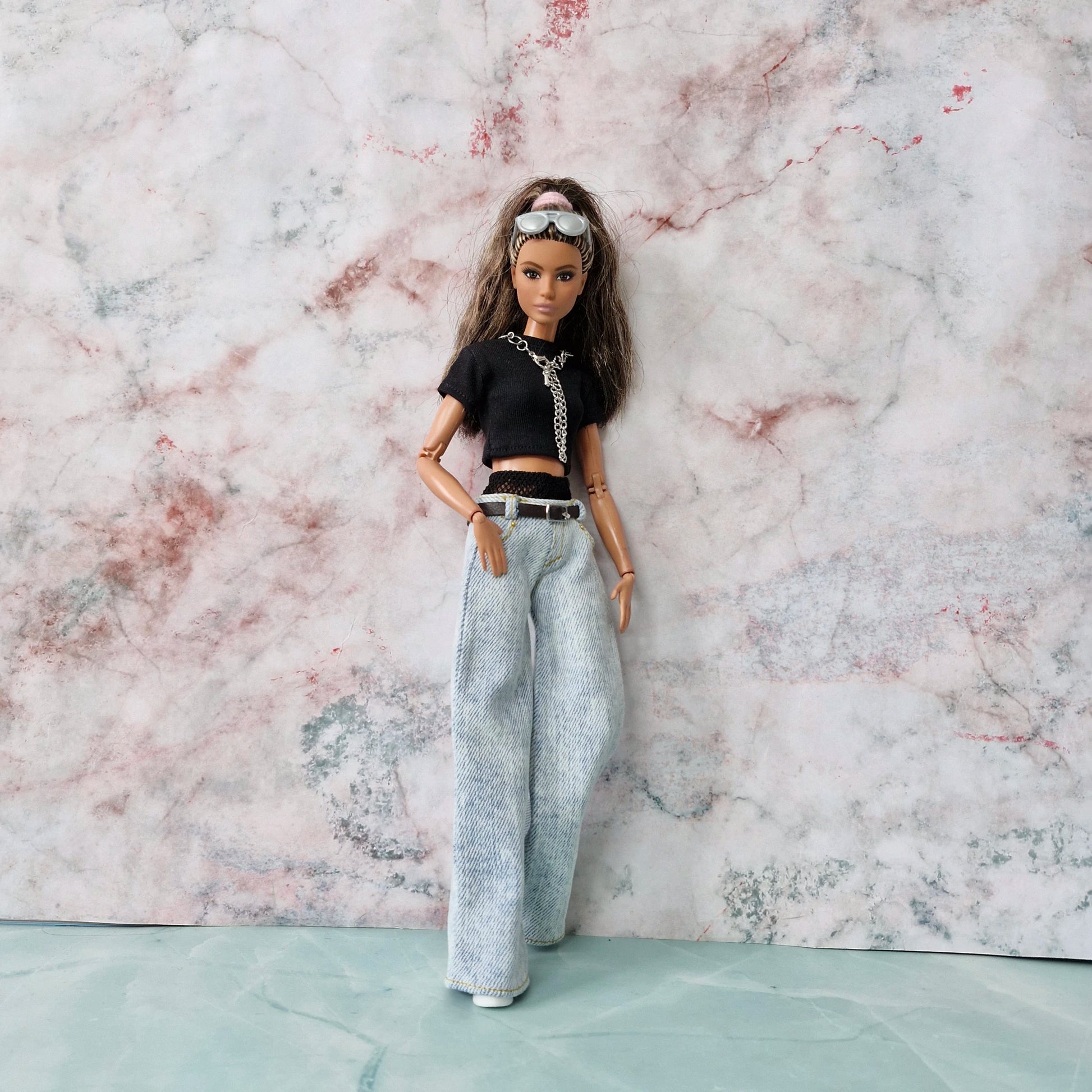 Full-length side view of Barbie doll in Y2K outfit with layered crop top and wide-leg jeans against a marble wall.