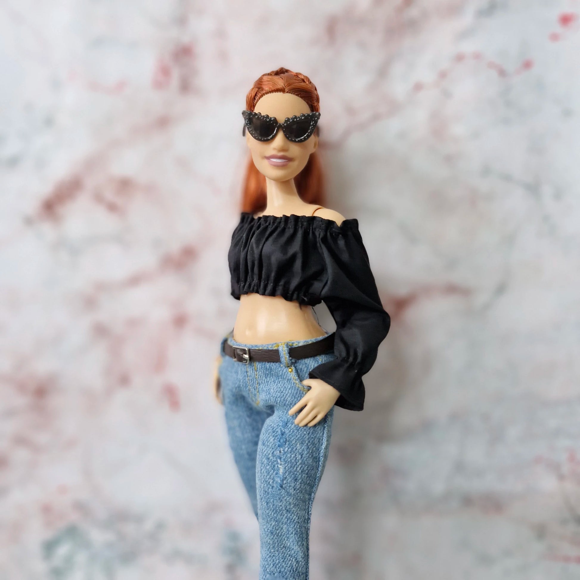 Side profile of Curvy Barbie doll in black off-shoulder top and skinny jeans, wearing black sunglasses.