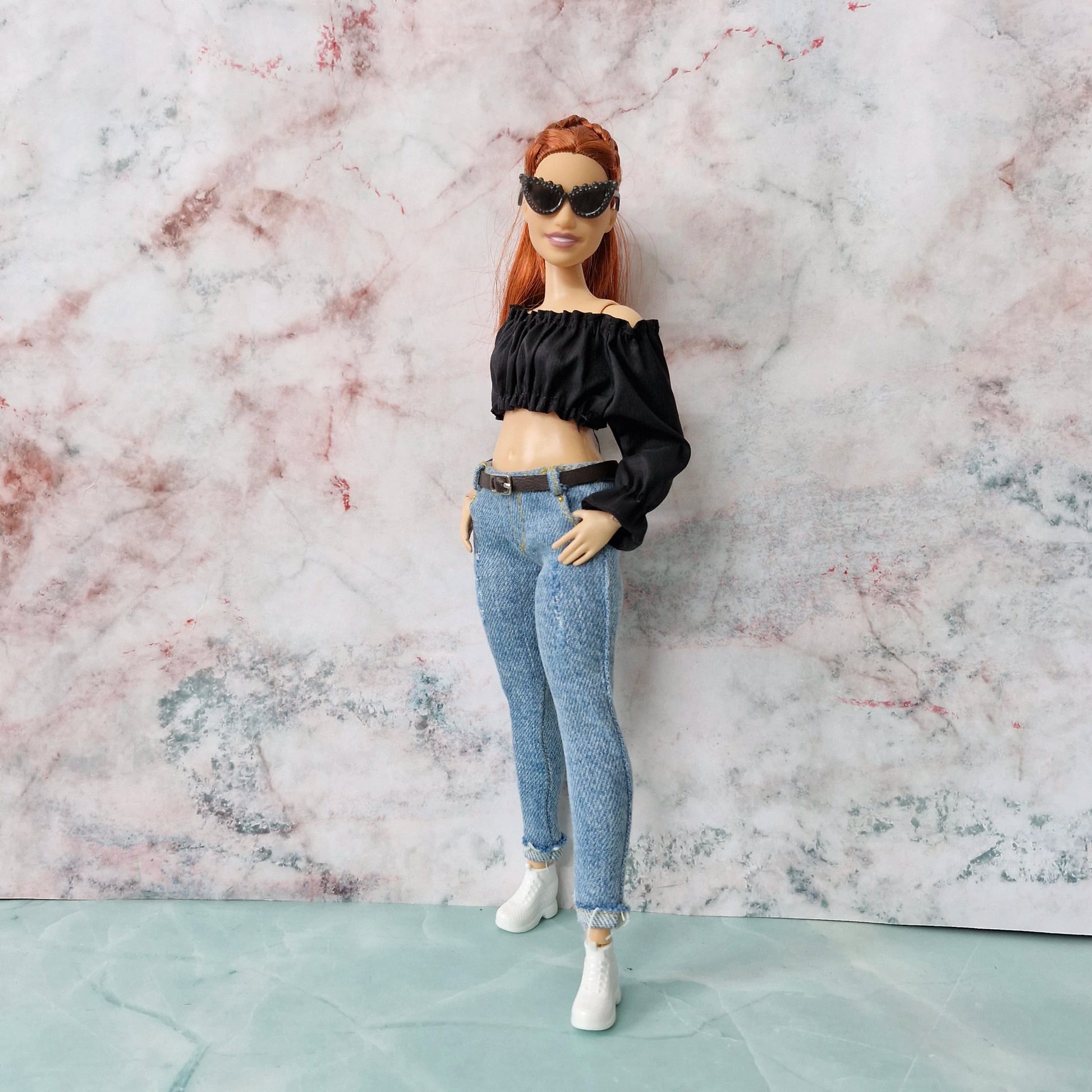 Full-length view of Curvy Barbie doll in edgy black crop top, skinny jeans, and sunglasses against a marble background.