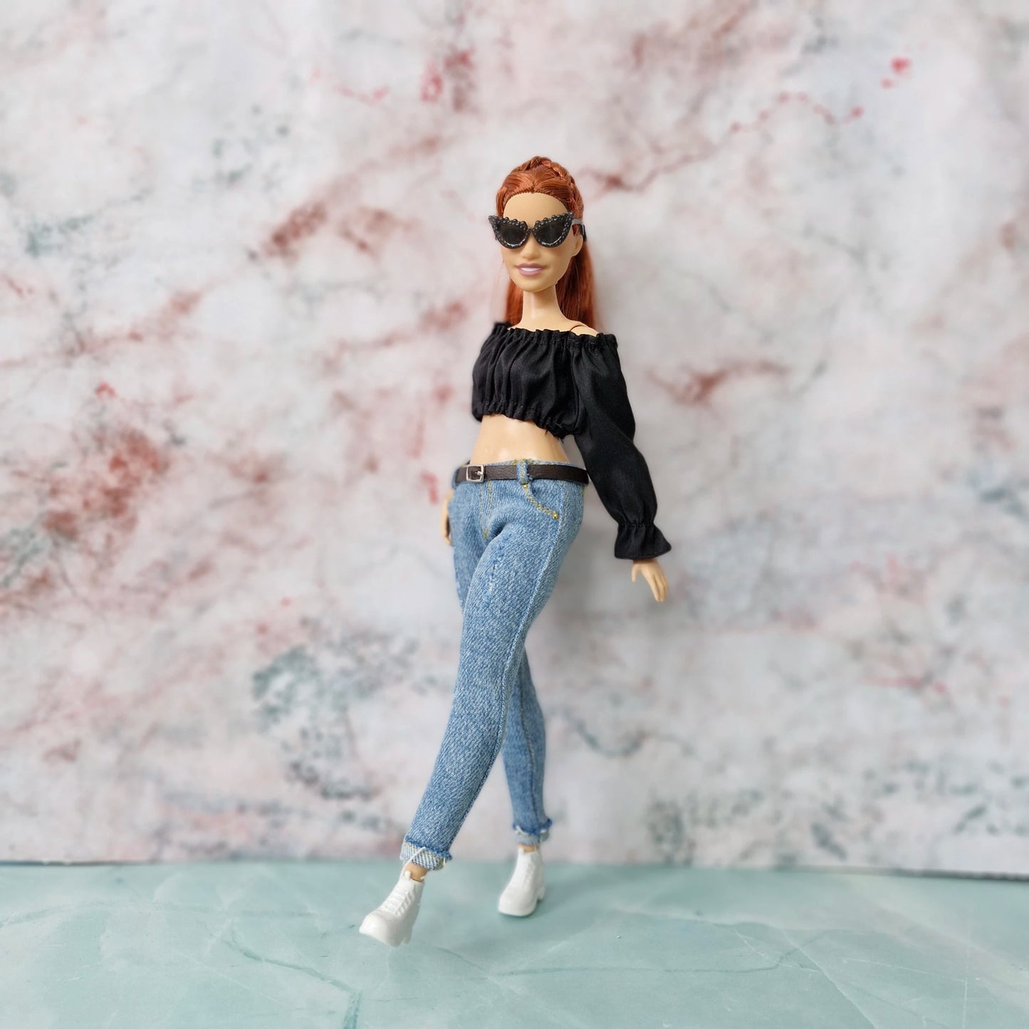 Curvy Barbie doll in black crop top and skinny jeans, posing with legs crossed while wearing sunglasses.