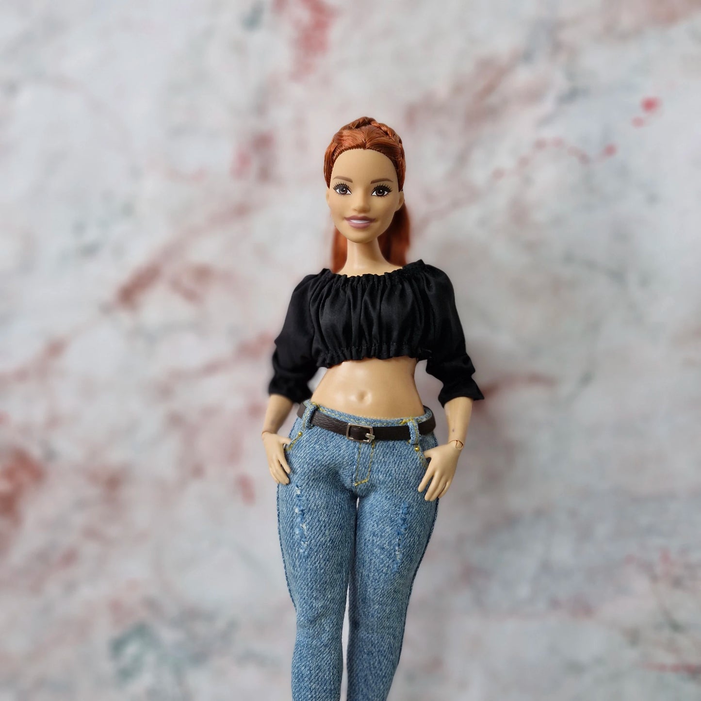 Curvy Barbie doll with red hair in black ruched crop top and light-wash jeans, smiling.