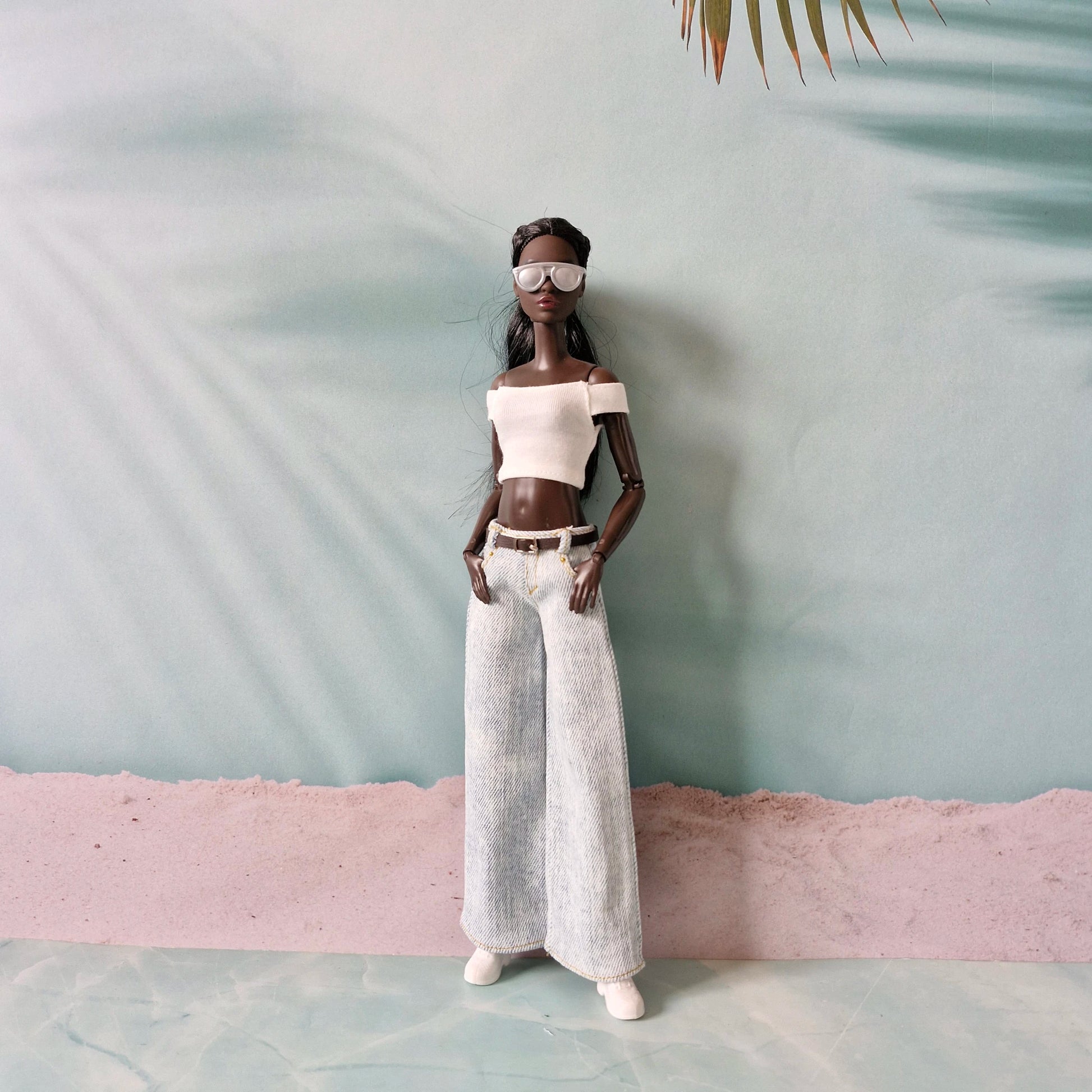 Doll wearing a white off-shoulder top and light-colored pants against a minimalistic background