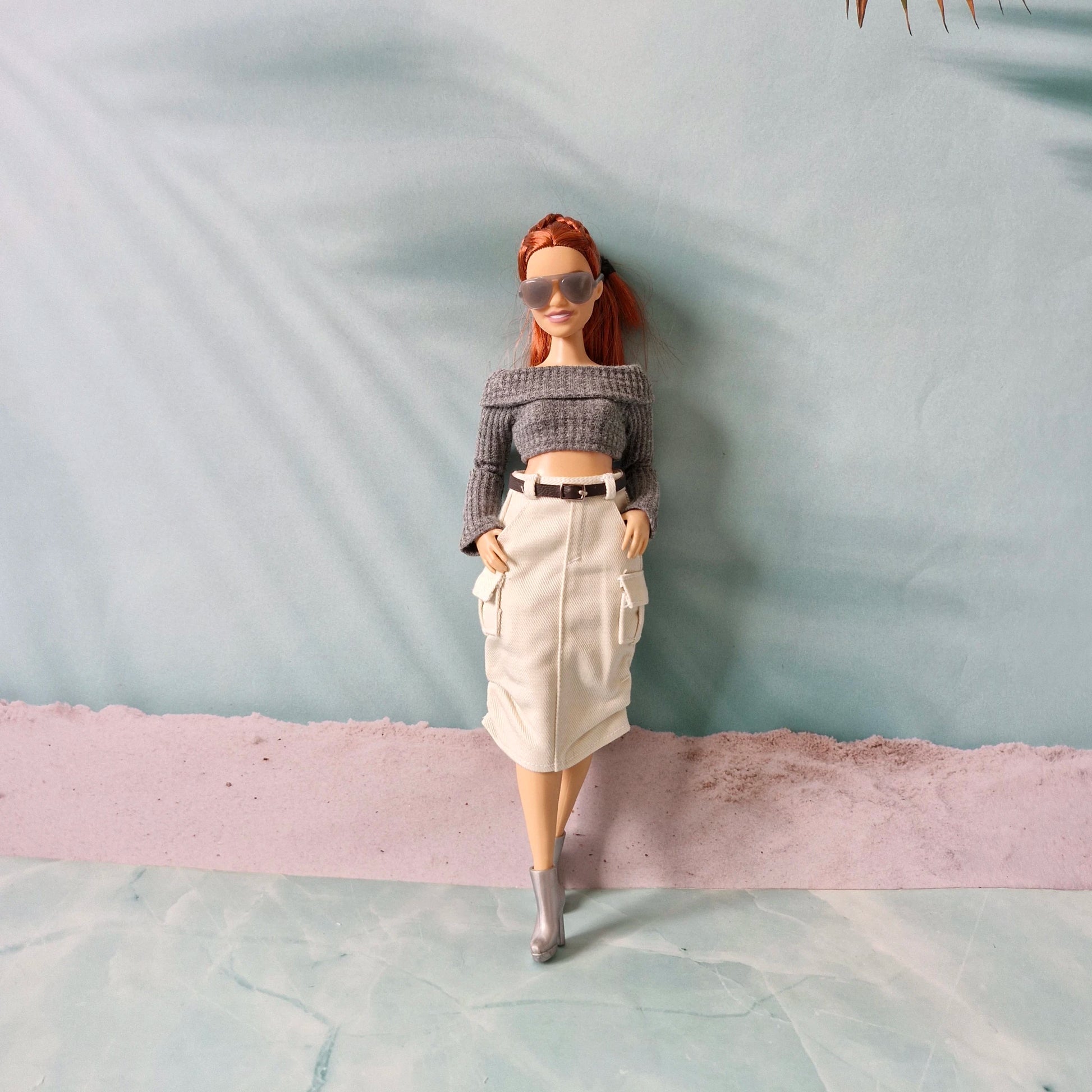 Barbie doll wearing sunglasses and a outfit against a textured light blue background