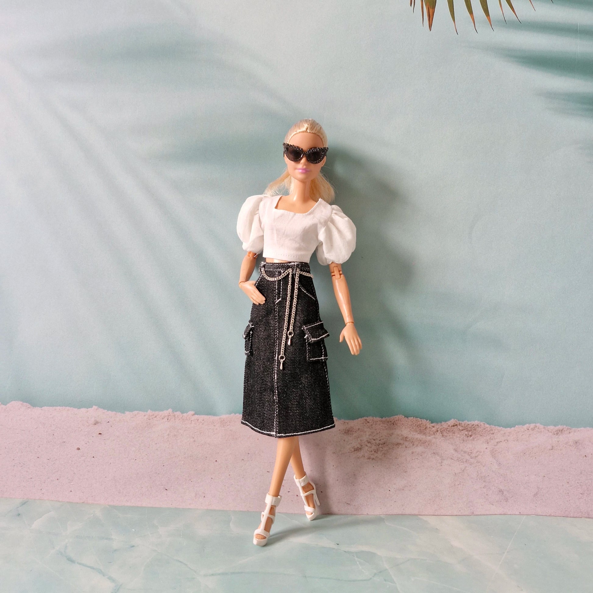 Barbie doll wearing a white top and black skirt with sunglasses against a light blue background