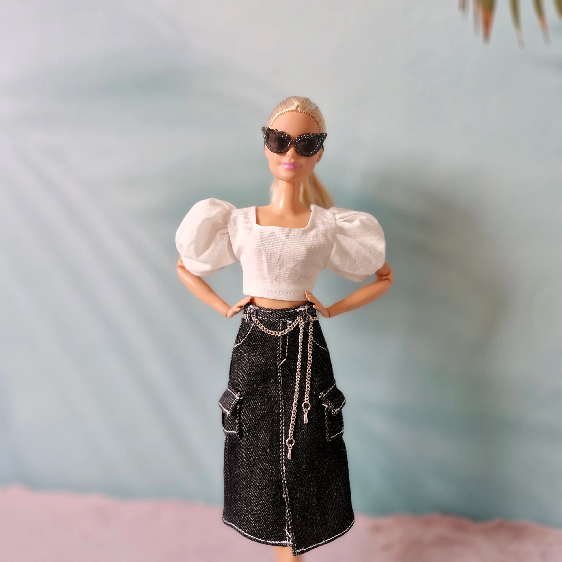 Barbie doll wearing a white top and black skirt with chains on a neutral background