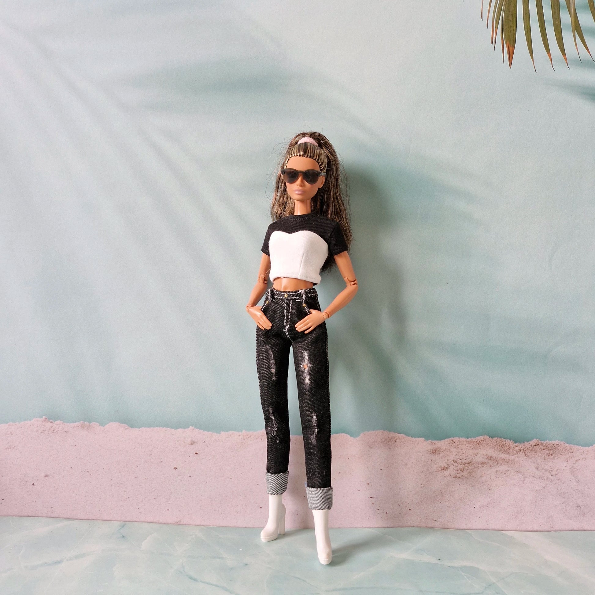 Barbie doll wearing a black and white top with ripped jeans on a beach-like setting