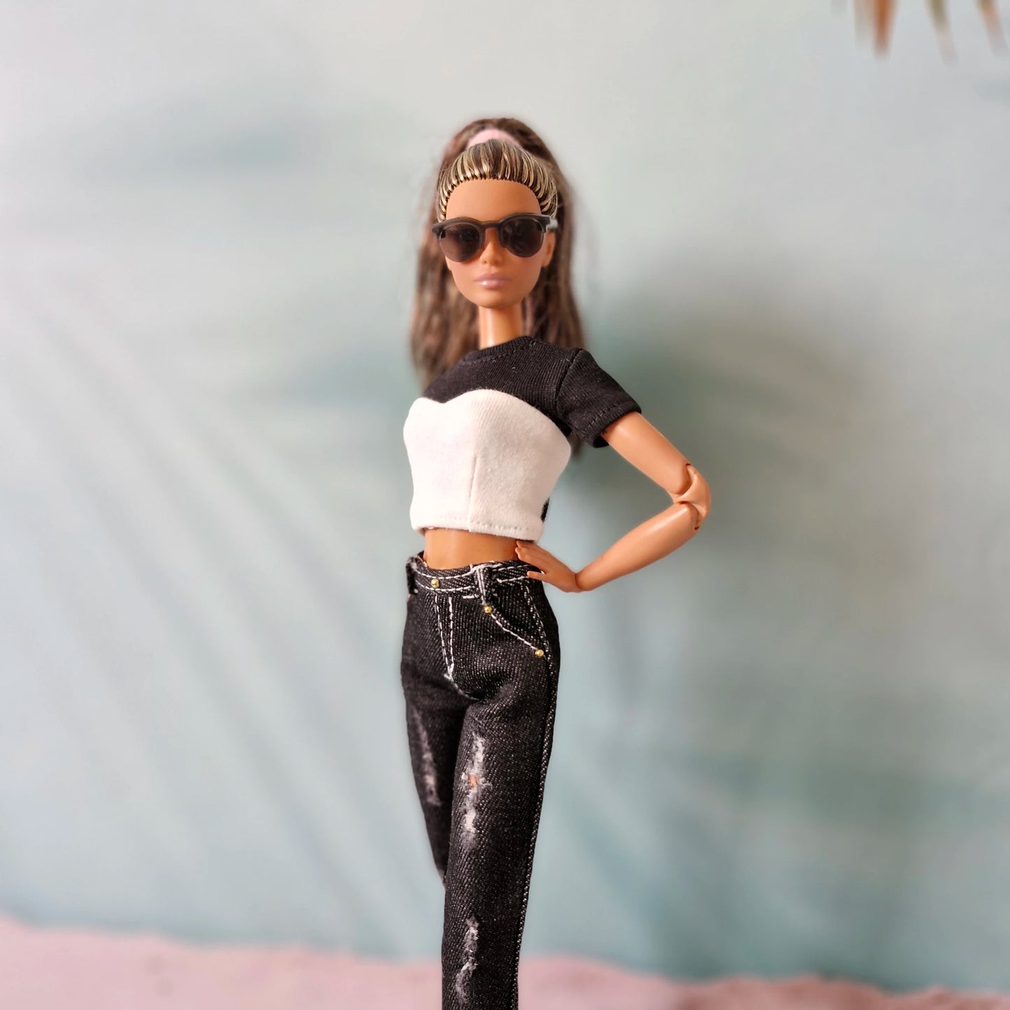 Barbie doll wearing a black and white top and black pants with sunglasses against a blurred background